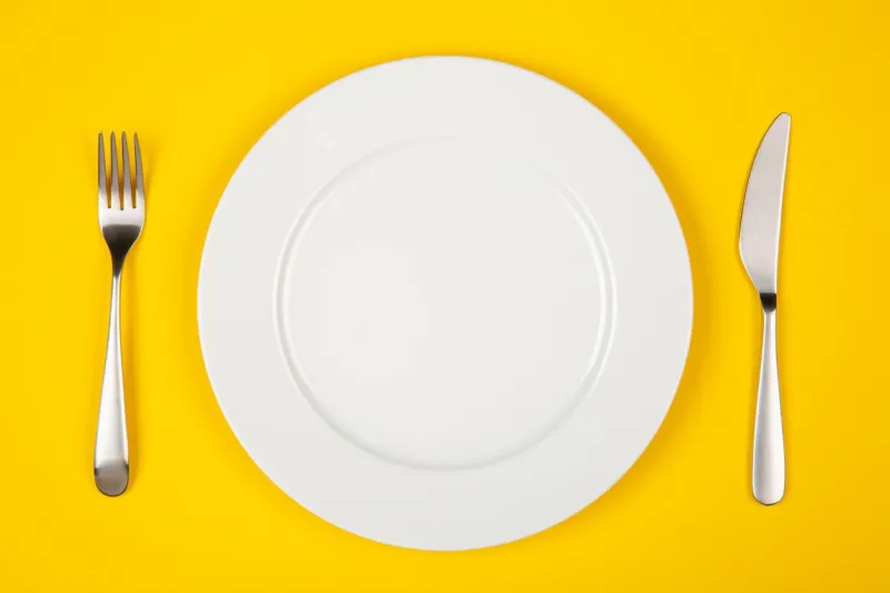 table setting with white plate, modern cutlery (fork and knife) on yellow table, top view, copy space