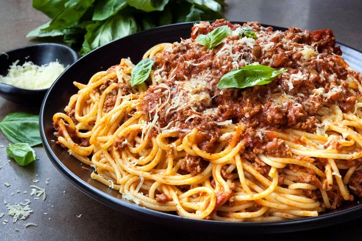 spaghetti bolognese in black serving platter, with fresh basil and parmesan