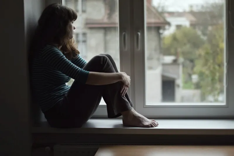 sad young woman sitting on the window, watching out