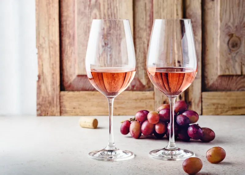 two glasses of rose wine and a bunch of grapes on a light wooden background