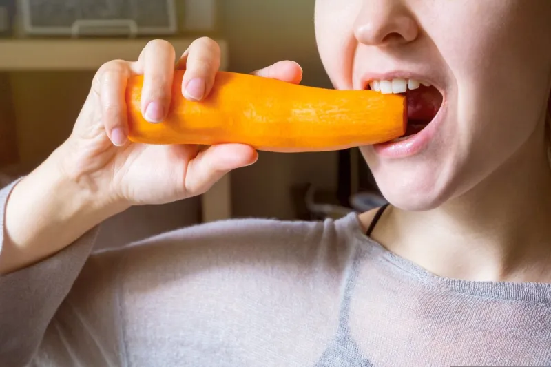 the girl nibbles a carrot she opens the mouth wide and shows healthy teeth the concept of healthy eating and veganism the focus on the carrot