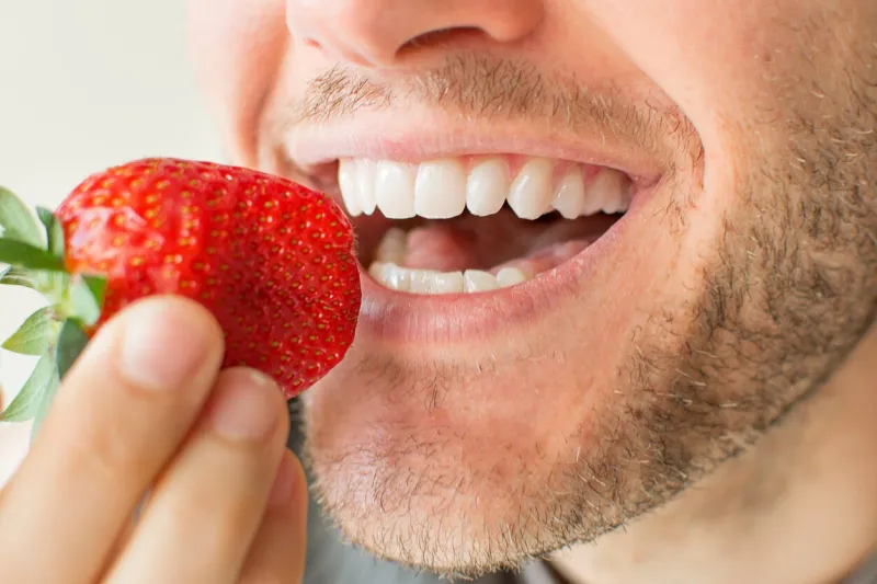 closeup of a man's face eating fruit with big smile