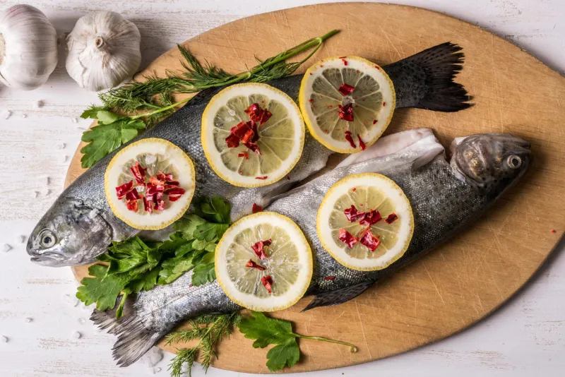 plat de poisson cuisson avec divers ingrédients truite arc-en-ciel cru avec le citron, l'ail, les herbes et les épices sur une planche à découper, vue de dessus des aliments sains ou un concept de nutrition diététique