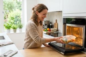 personne qui met un contenant en plastique dans le micro-ondes.