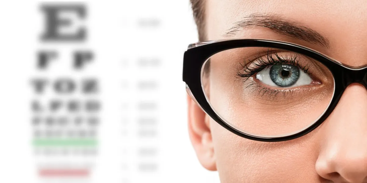 close up of young woman wearing eyeglasses with eyechart in the background