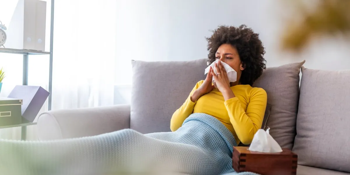 the sick woman, holding a handkerchief, sneezing and feeling freezing, lying on the bed, at home health problem sick african american woman lying on the sofa