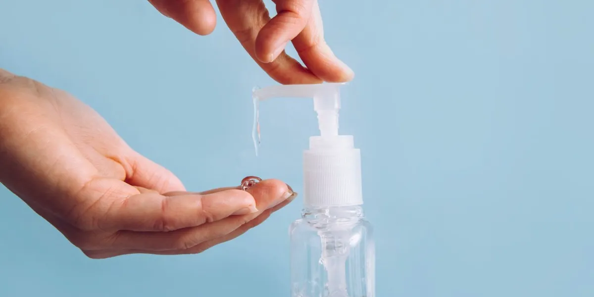 close up view of woman using hand sanitizer dispenser, blue clean minimalist background health concerns concept