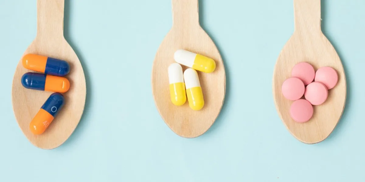 assorted pharmaceutical medicine pills, tablets and capsules in wooden spoon on blue background helthcare