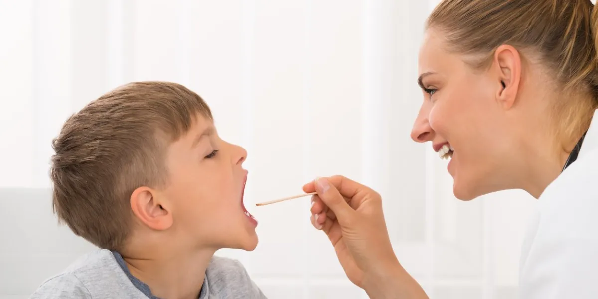 female doctor examining little boy's mouth in clinic