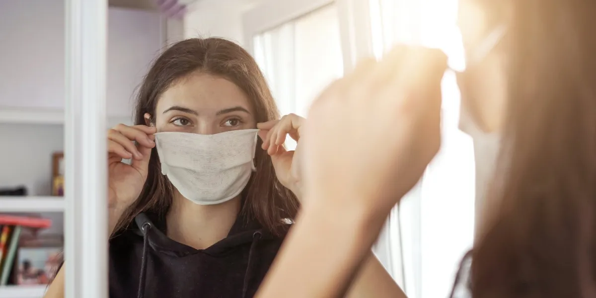 young girl wearing medical protective face mask looking mirror stay at home social dictancing concept