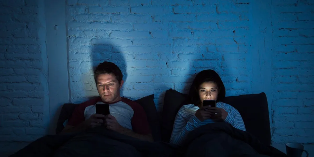 young couple at home in bed late at night using mobile phone in relationship communication problem and internet social media network concept