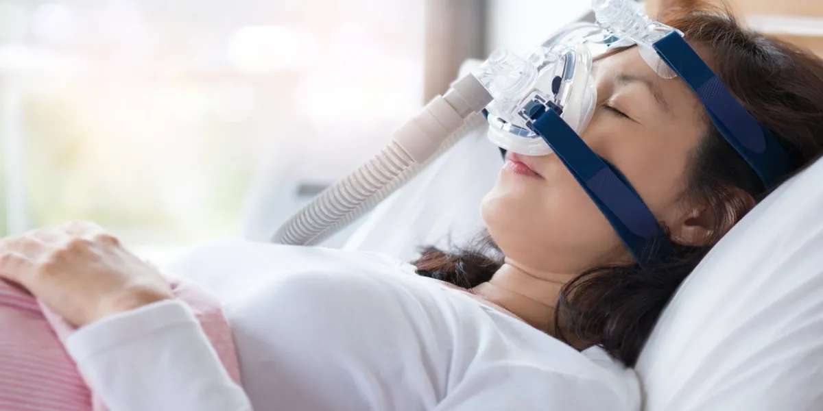 senior woman using cpap machine to stop choking and snoring from obstructive sleep apnea with bokeh and morning light background