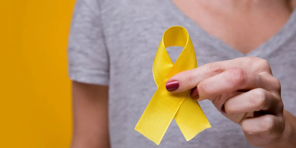 young female holding yellow gold ribbon awareness symbol for endometriosis, suicide prevention, sarcoma bone cancer, bladder cancer, liver cancer and childhood cancer concept health care close up