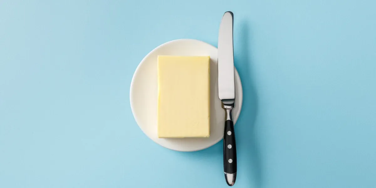 top view of butter and knife on white plate on blue background