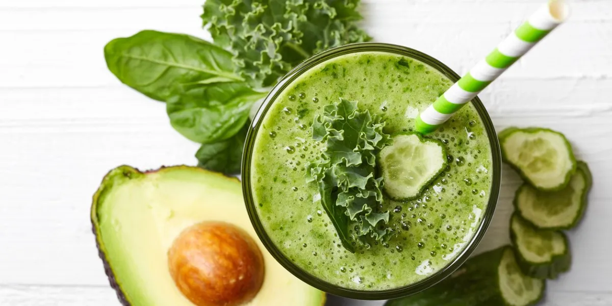 glass of green vegetable smoothie on white wooden background from top view