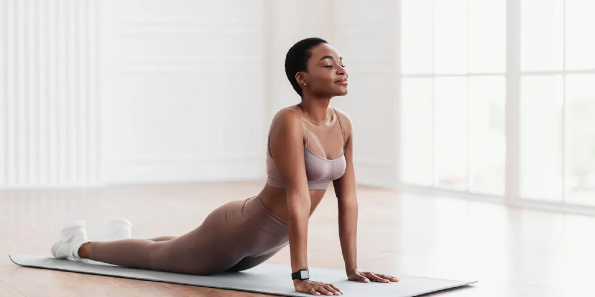 relief lower back pain smiling black woman doing sphinx cobra pose or upward-facing dog asana stretching back muscles practicing pilates, excercising at fitness studio or in living room on yoga mat