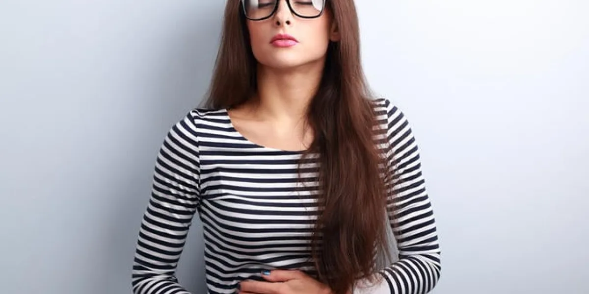 belle femme d'affaires stressée à lunettes souffrant de douleur à l'estomac sur fond bleu