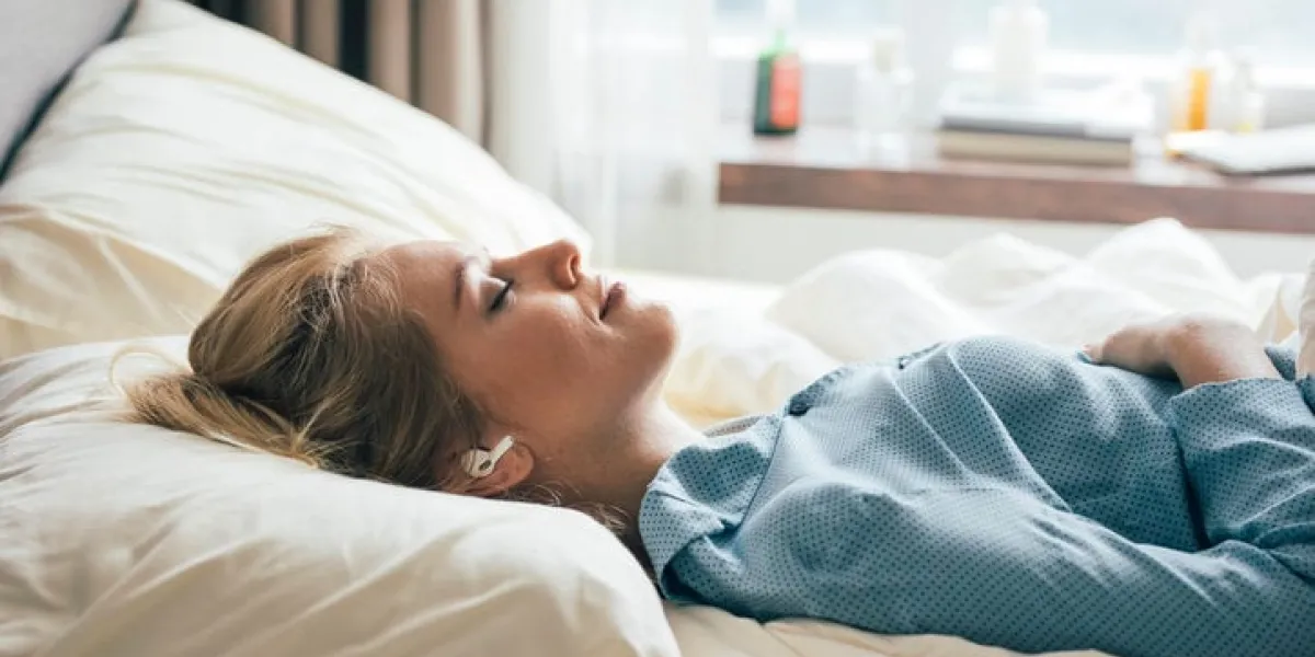 happy blonde woman in blue pajamas lying in bed in the morning and listening to relaxing music