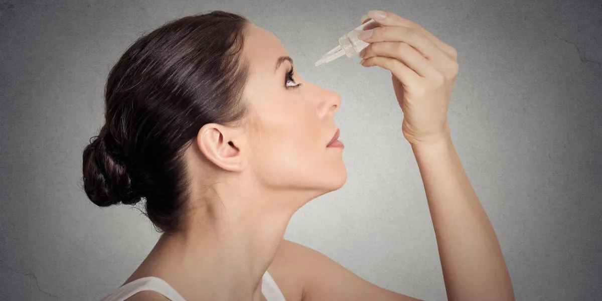 jeune femme de profil côté, appliquer des gouttes pour les yeux isolés sur fond de mur gris