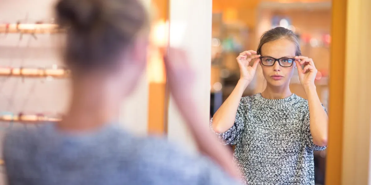 jolie, jeune femme choisissant de nouveaux cadres de lunettes dans un magasin d'opticien (couleur image tonique, dof peu profond)