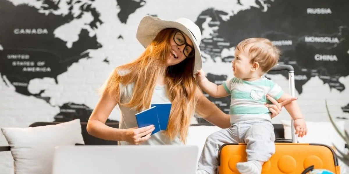 happy and playful woman with baby boy sitting at the travel agency office with beautiful map on the background ready for a summer vacation