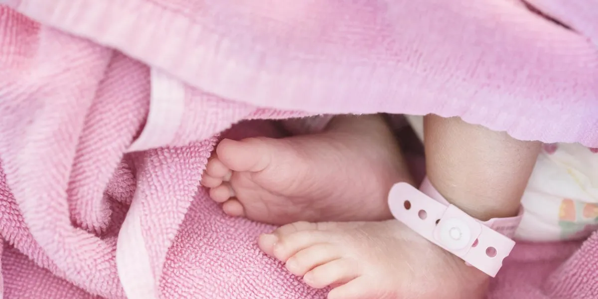 closeup foot of baby with newborn ankle tag on bed in hospital textured background