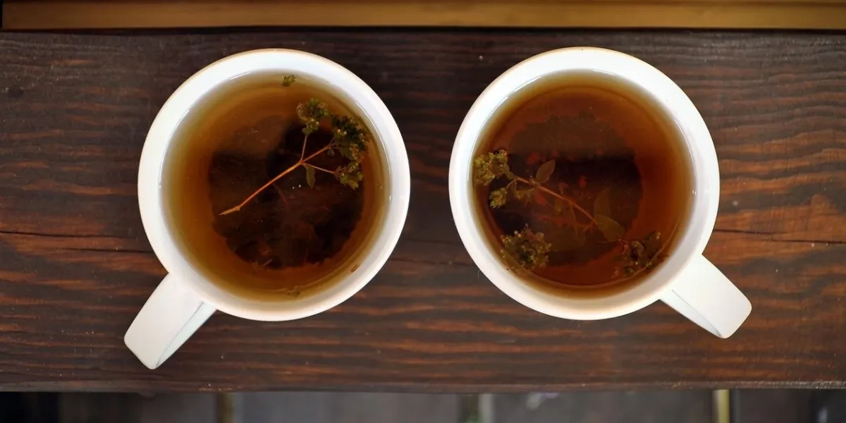 top view of two white cups with black tea and thyme on a dark wooden surface