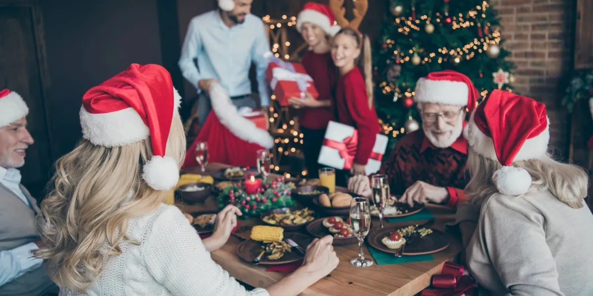 merry x-mas noel meeting of large family back side photo old people sit table speak talk eat feast wear red santa claus cap hat father have fun with small little boy son near christmas tree garlands