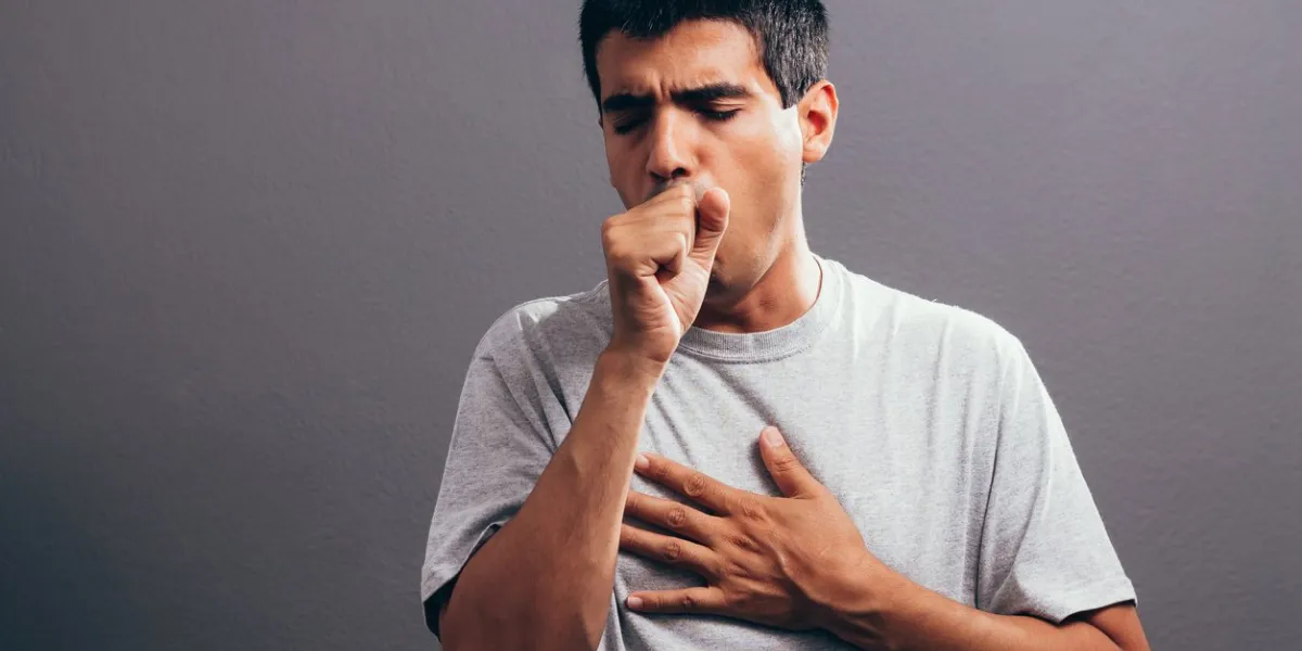 man coughing into his fist, isolated on a gray background