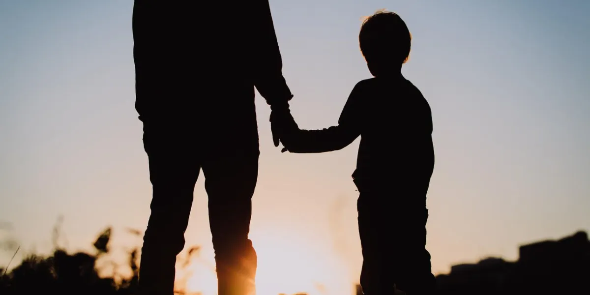 silhouette of father and son holding hands at sunset sky