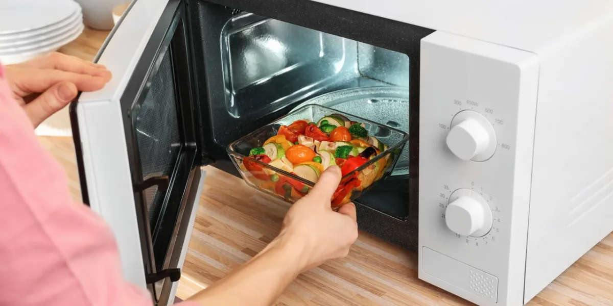 woman putting bowl with vegetables in microwave oven, closeup