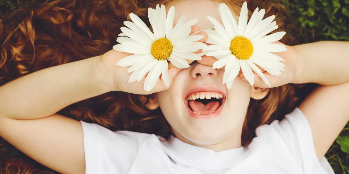 child with daisy eyes, on green grass in a summer park