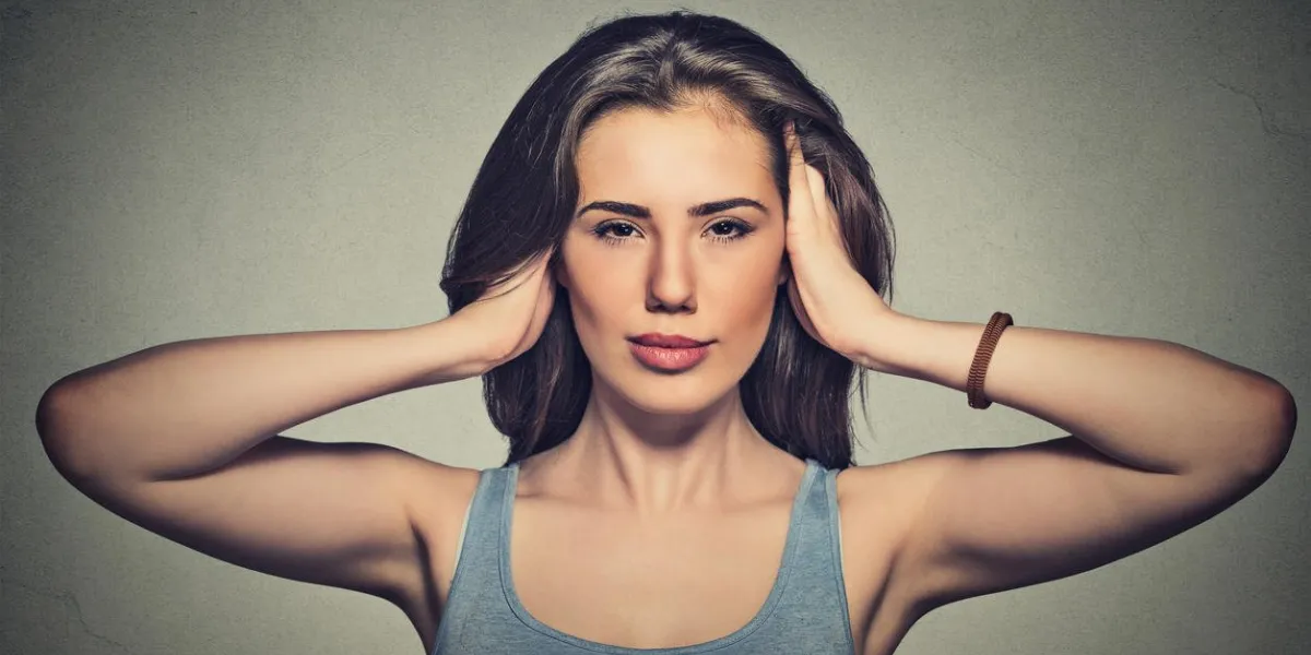portrait of young attractive casual woman covering with hands her ears eyes opened isolated on gray wall background hear no evil concept