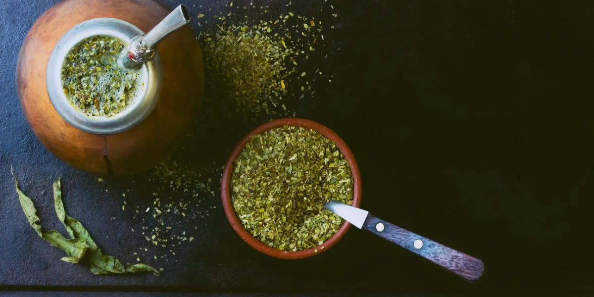 yerba mate en calebasse et herbe sèche dans un bol en argile sur fond noir vue de dessus