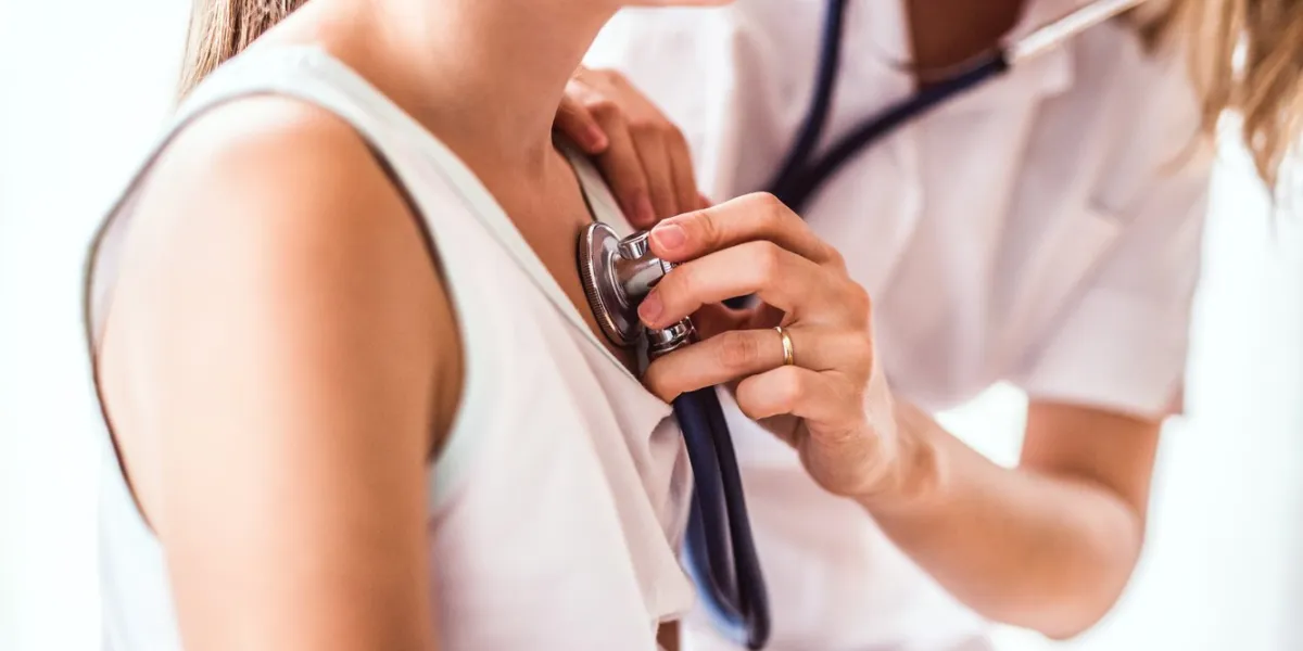 unrecognizable young female doctor examining a small girl with stethoscope in her office close up