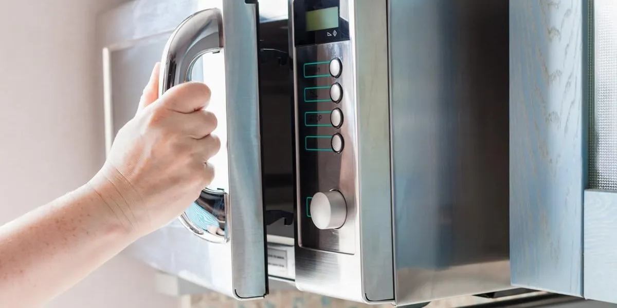 la main ouvre la porte du four à micro-ondes pour chauffer les aliments