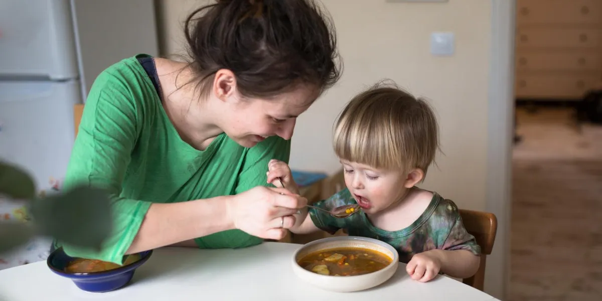 mère nourrit la soupe enfant dans la cuisine lumineuse à la maison, intérieur réel, maman avec des dreadlocks, occasionnel