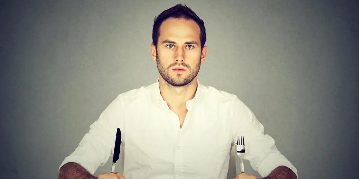 man with fork and knife sitting at table with empty plate
