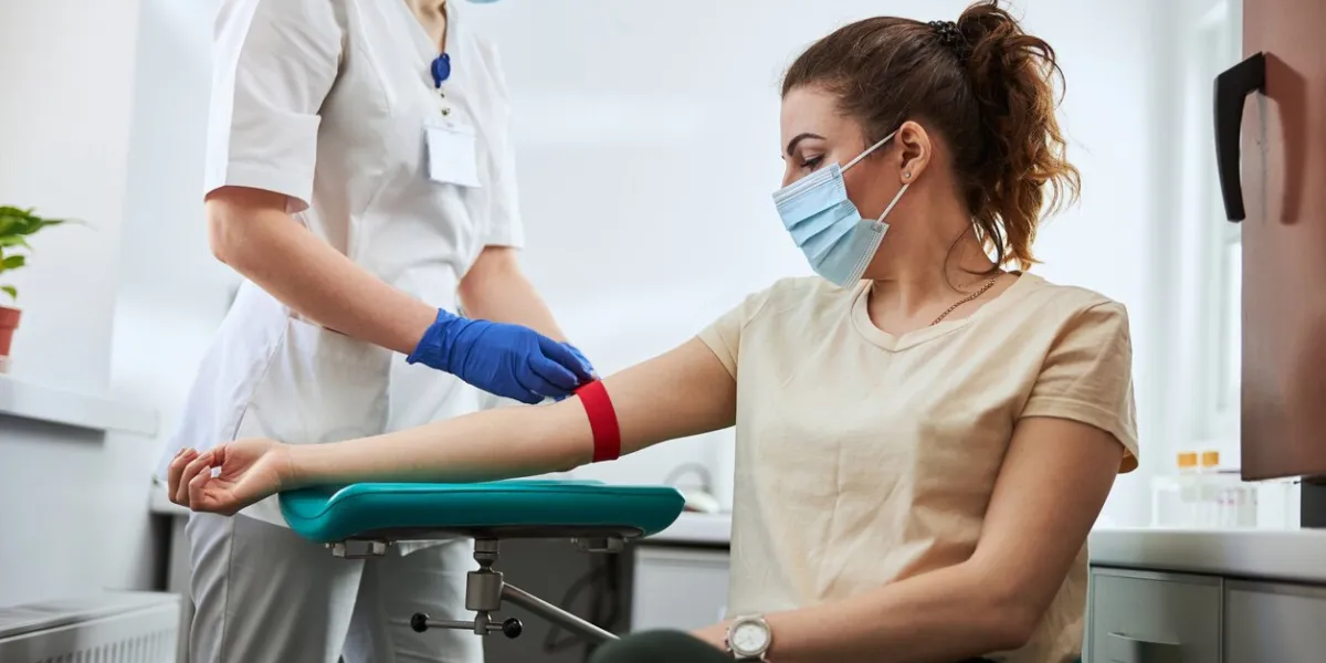 skilled focused young phlebotomy technician applying a tourniquet to a female patient arm for venipuncture