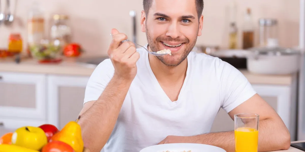 beau jeune homme ayant un petit déjeuner sain tout en restant assis dans la cuisine