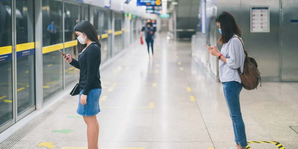 two young asian woman wearing protective face mask stand in line with social distancing during waiting train in subway due to coronavirus or covid-19 outbreak situation in all of landmass in the world