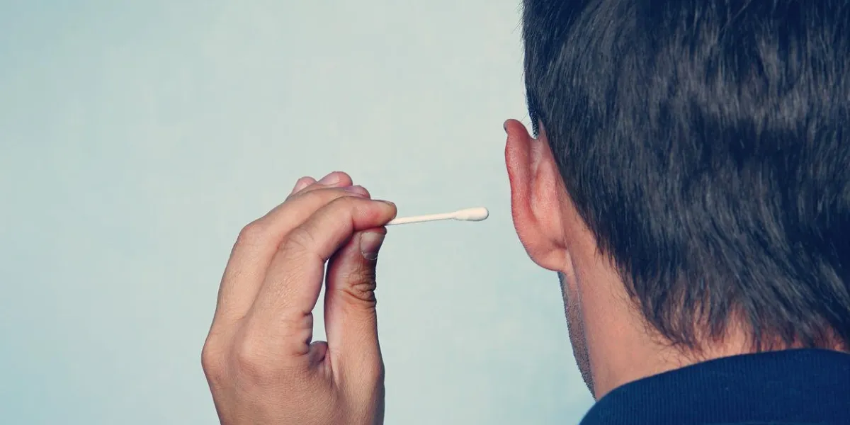 happy man cleans his ear with a cotton swab close-up on blue background