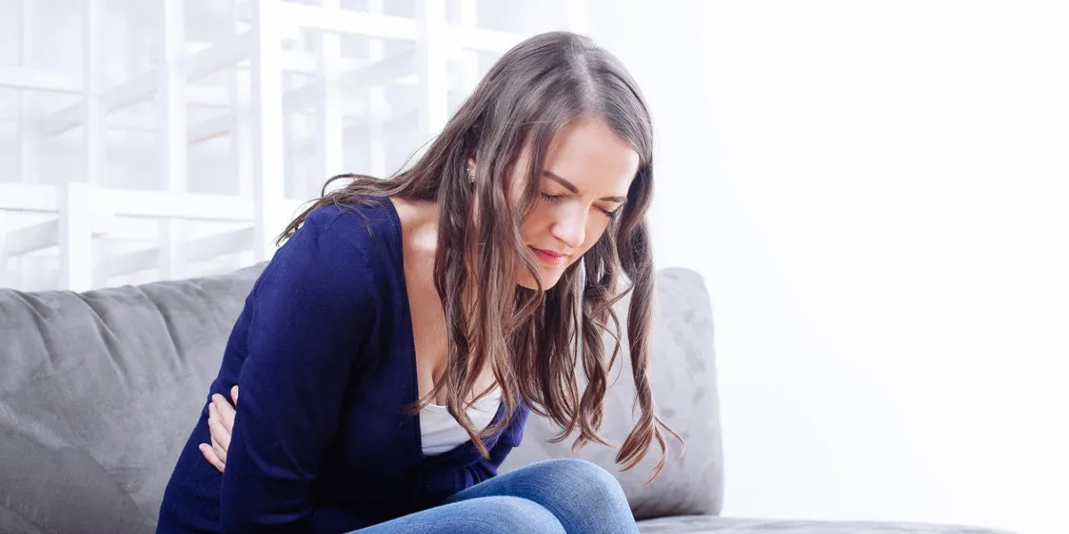 jeune femme assise sur un canapé souffrant de maux de ventre à la maison