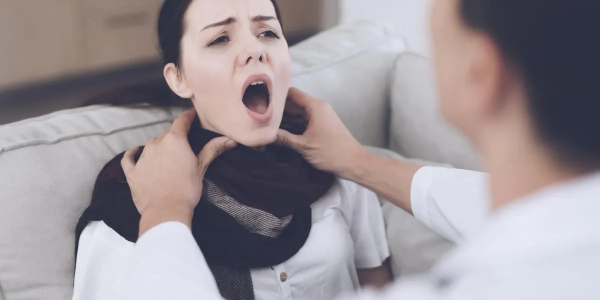 the woman fell ill and called the doctor at home she sits on the sofa with a blanket doctor in a white coat examines her throat
