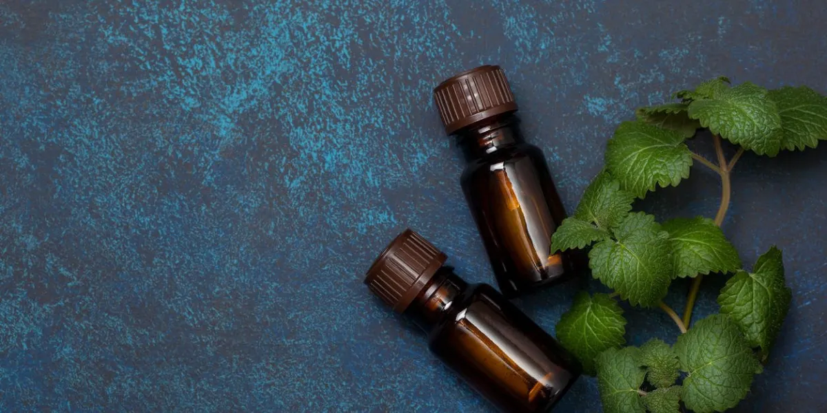 huile essentielle de menthe dans une bouteille en verre, brins de menthe fraîche sur fond bleu