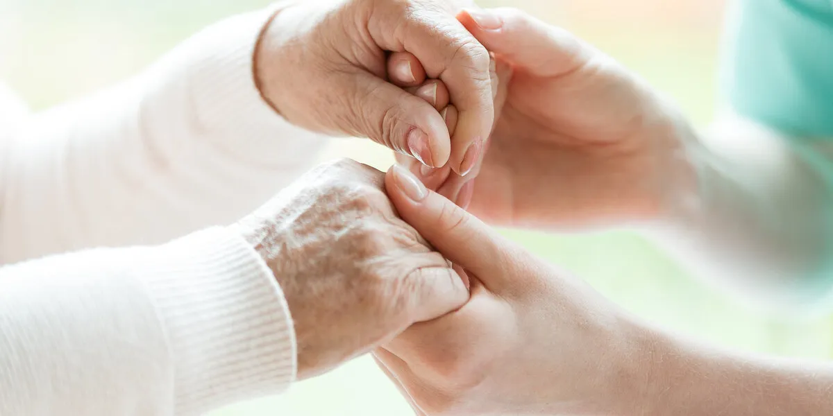 closeup of the hands of a young woman holding hands of an elderly lady