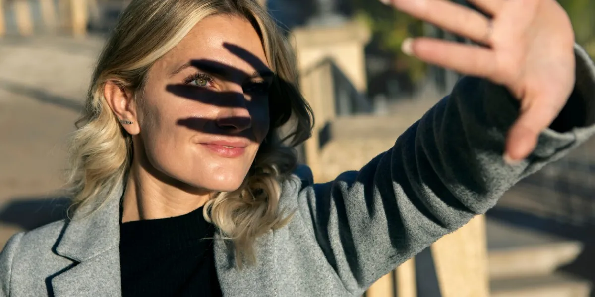 portrait of blonde woman facing the sun making shadow with her hand on her face revealing a green eye