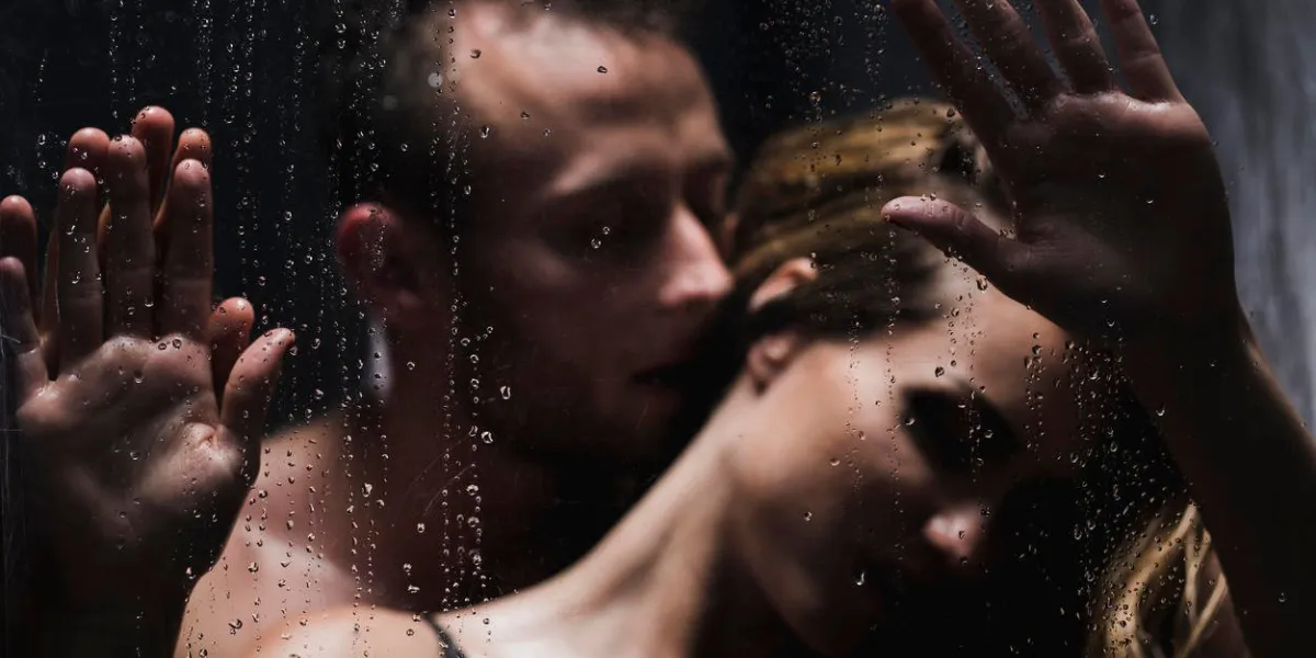 man whispering to woman's ear with his hands on glass shower during foreplay