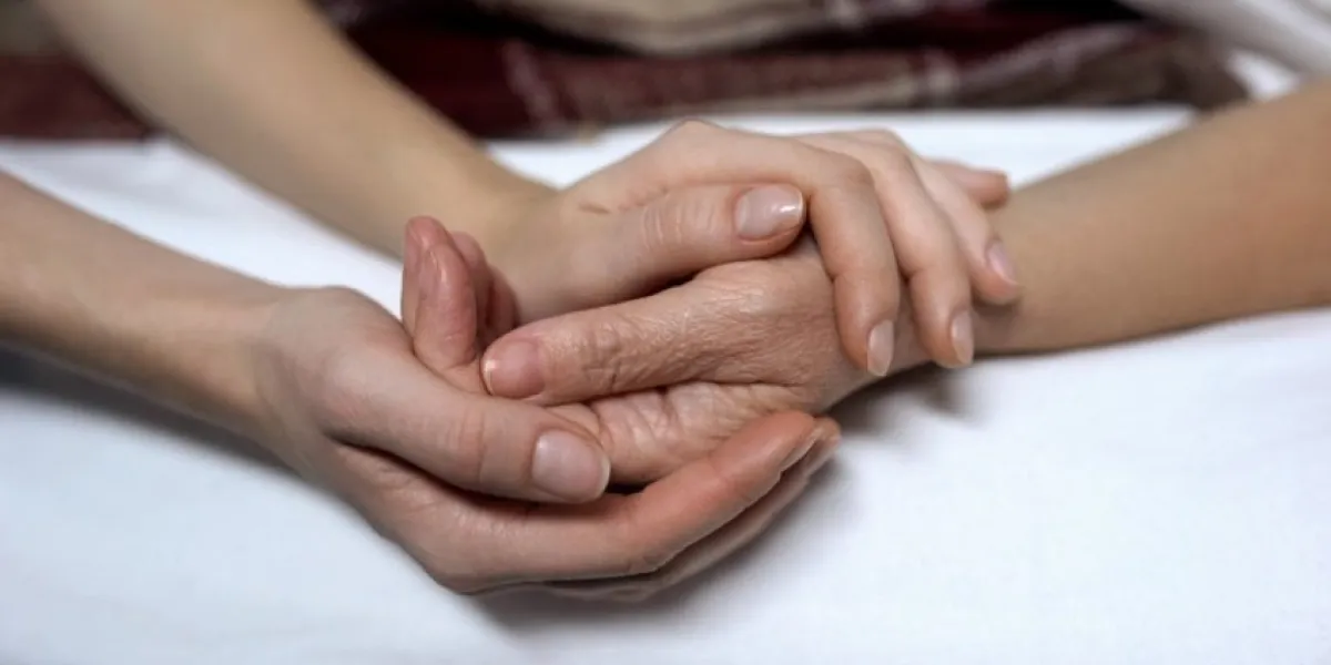 warm daughters hands holding and calming down sick mother in bed, assistance