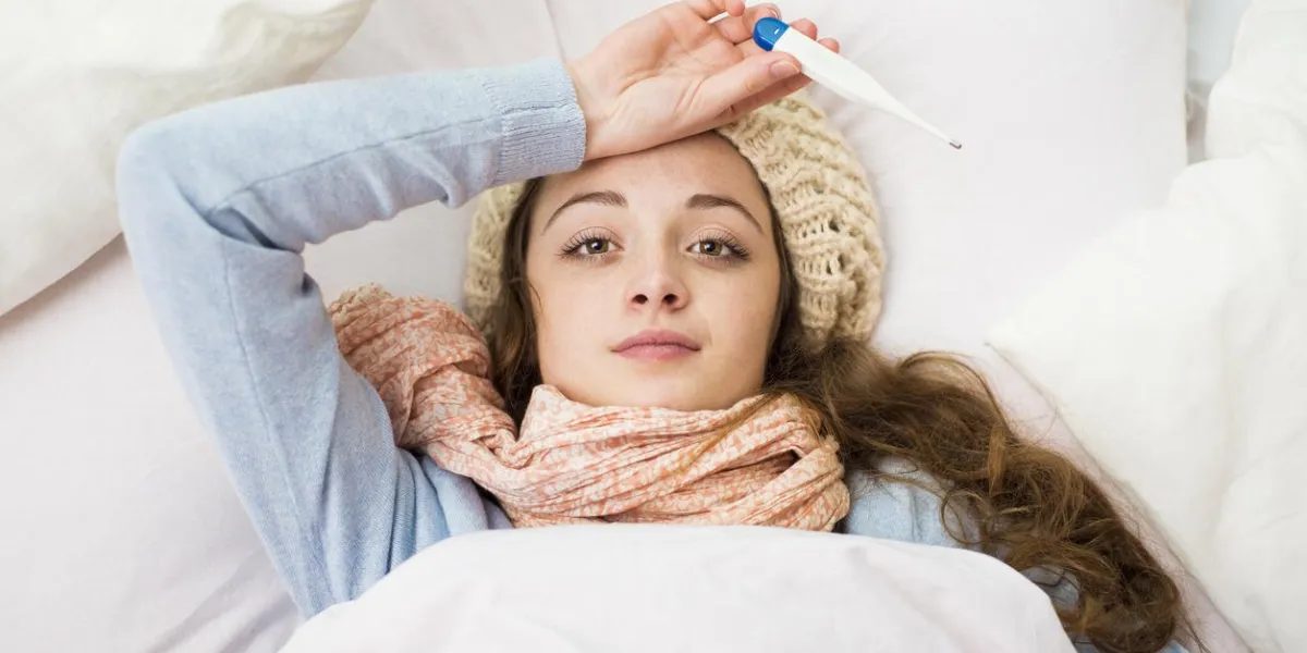femme malade avec un thermomètre est couché dans son lit, elle a le rhume, la grippe et une forte fièvre